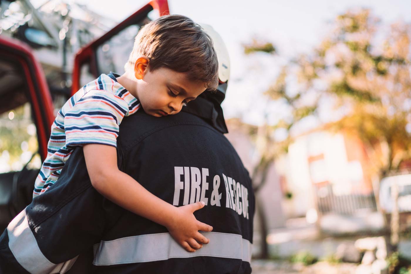A boy is hugging an adult firefighter.